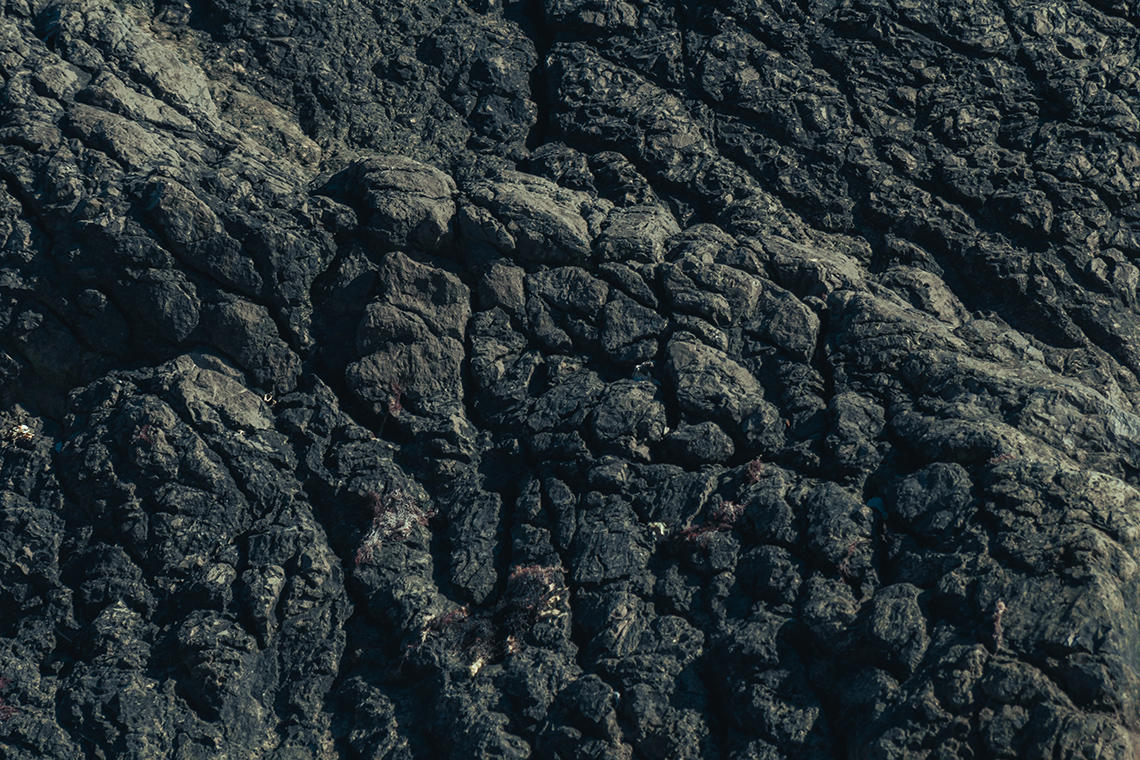 Dark grey rock with many fissures and bumps.
