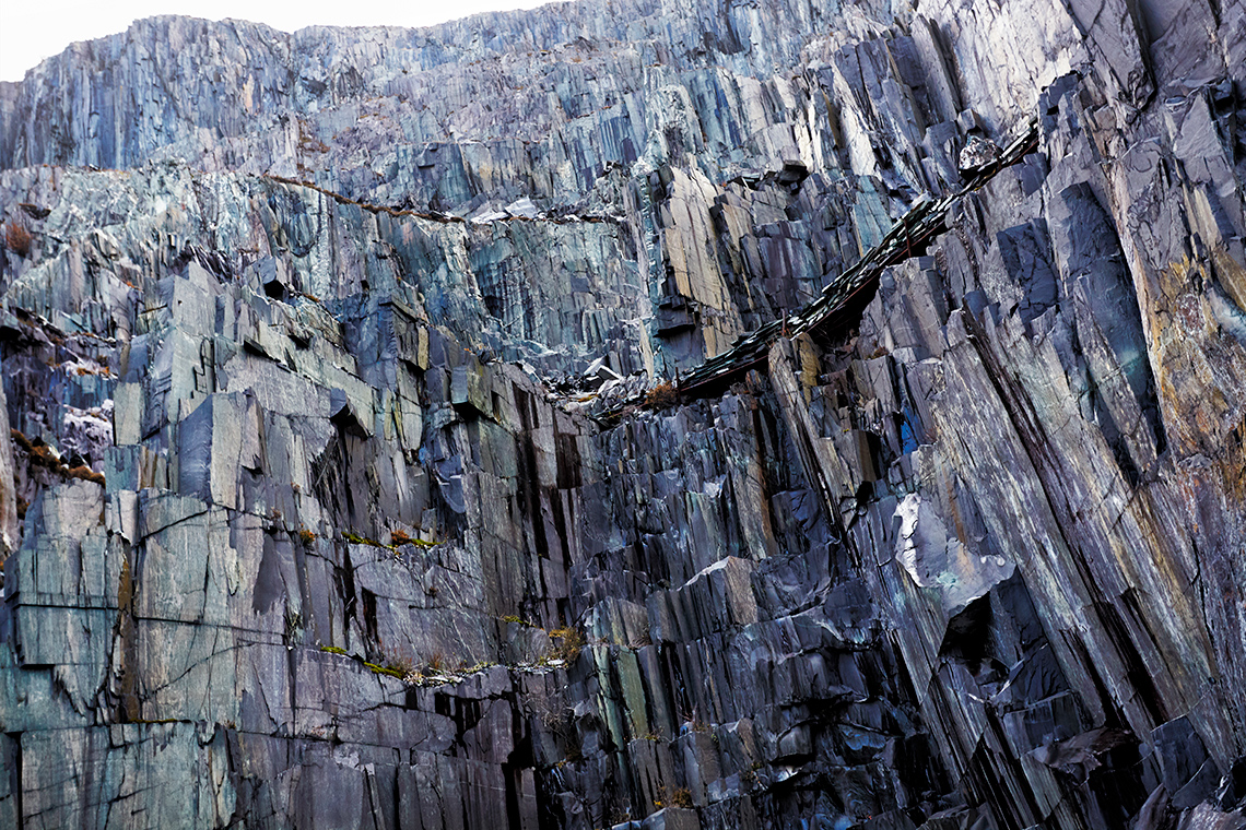 A rocky cliff is covered in slate, a metamorphic rock. It has layers that look like ribbons and have a shiny appearance.