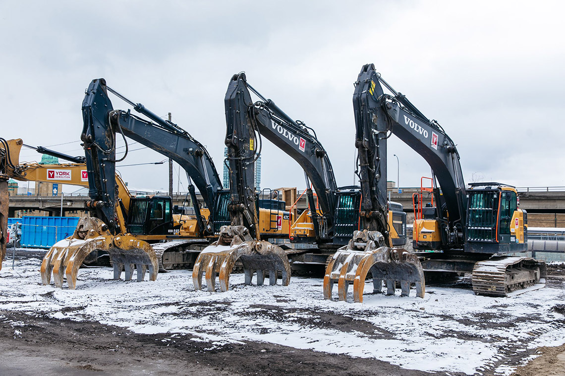 Three Hy Hoe Excavators sit at a construction site lined up in a row ready to break ground on the construction of new Toronto subway lines.
