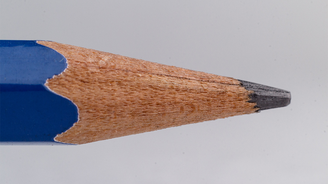 A close-up view of the tip of a pencil showing the part of the painted shaft, wood tip, and graphite pencil lead.