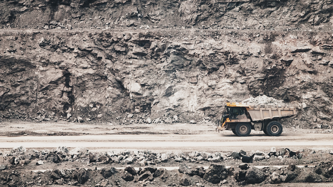 A large dump truck moves rocks, dirt, and minerals along a road inside an outdoor open pit mine.