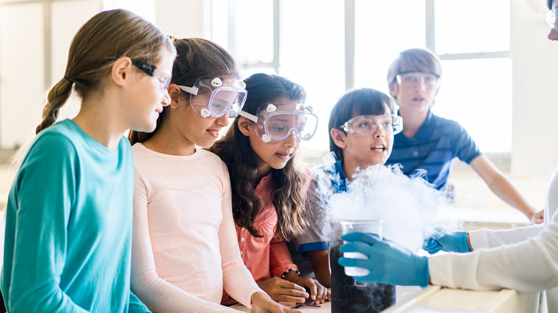 Students wearing goggles and looking at beakers filled with liquid.