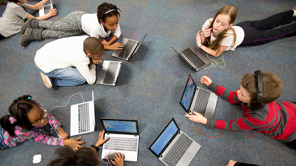 Students using technology and devices in the classroom, like a laptop.