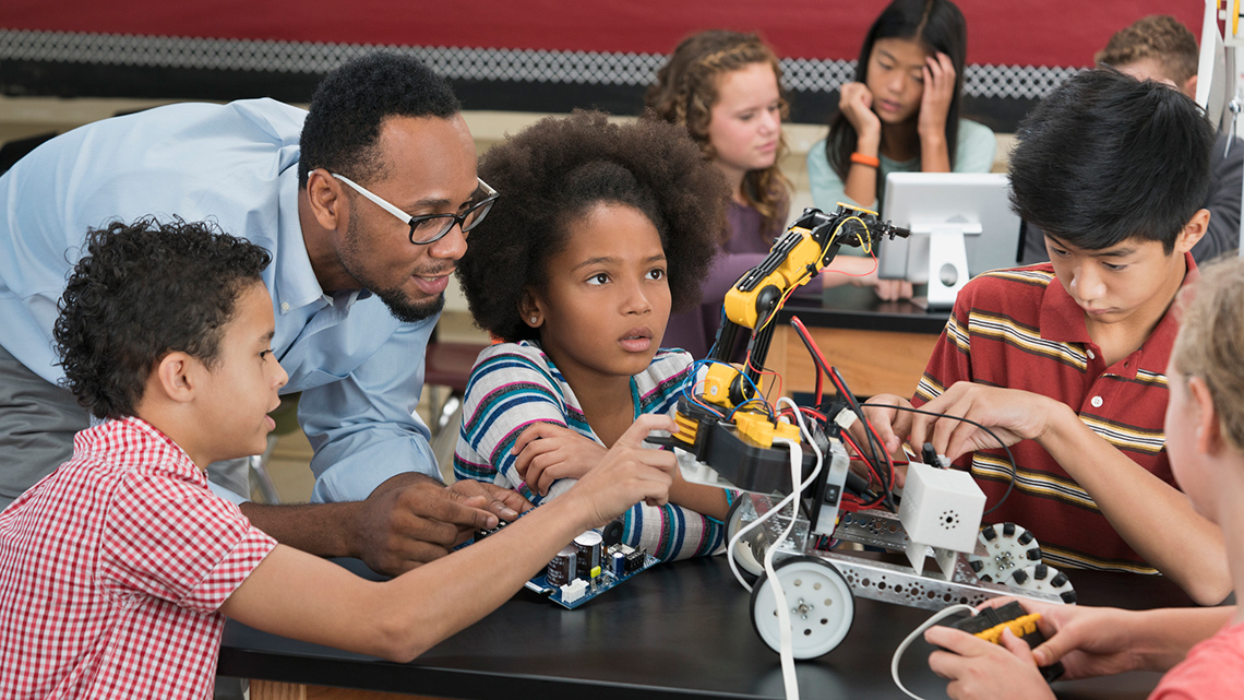 Teacher and students tinkering with a robot.