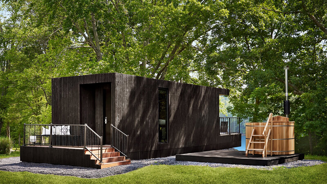 One storey black prefab house with windows, doors, stairs, and a deck.