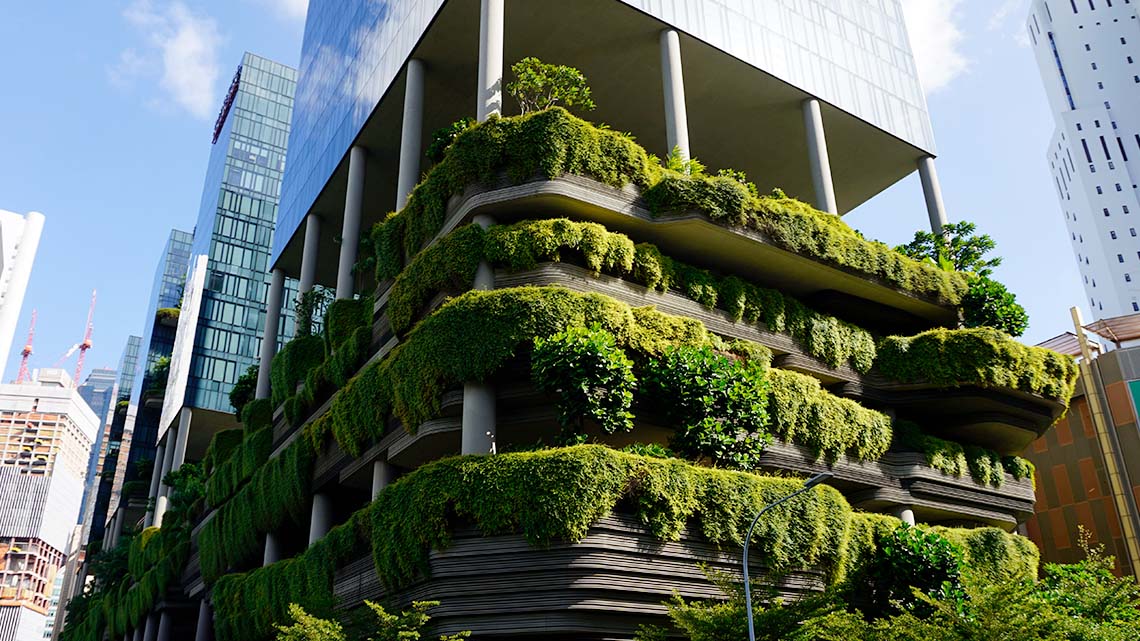 An office building with trees and plants growing on and over the balconies of lower floors.