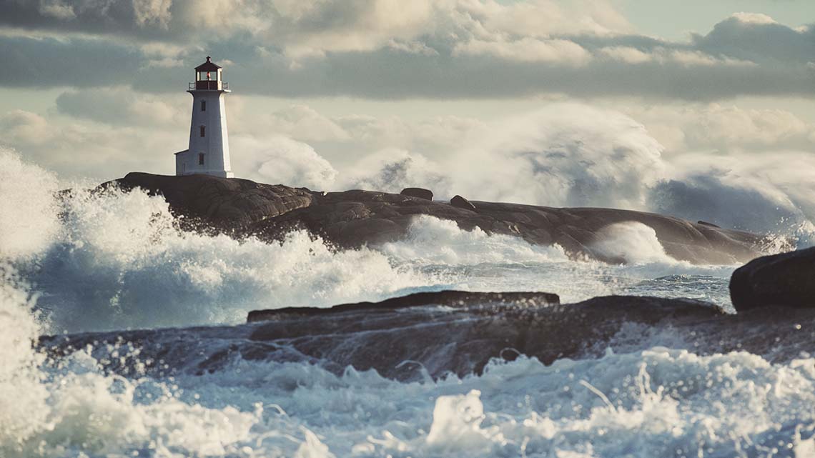 Waves crashing against rocks with a lighthouse at the top.