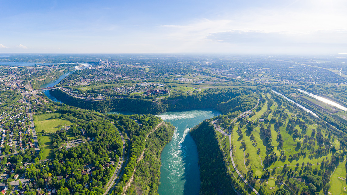 An aerial view of the town surrounding Niagara Falls. A body of water cuts through the land creating a zig-zag pattern.