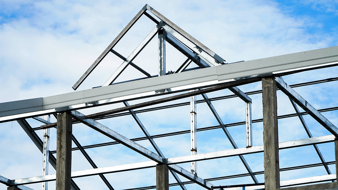 A metal frame of a roof sits atop the structure of a house. The roof is designed as a truss.