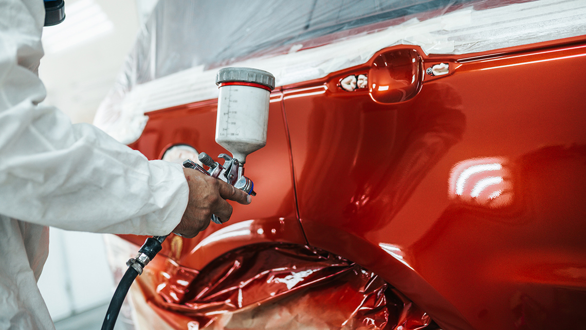 A person paints a car using spray paint.