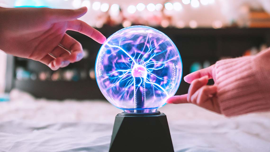 A plasma ball with different colours. People touching the plasma ball with their fingers