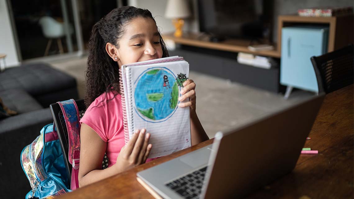 A student holding their notebook up to a computer screen to share the picture they drew of the earth.