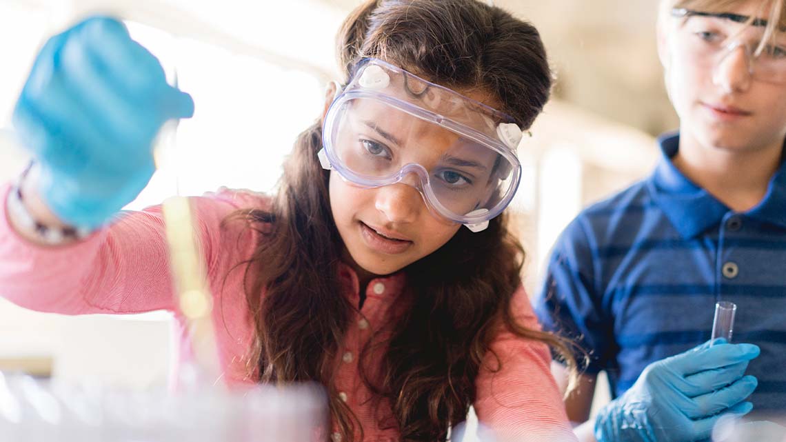 Two students wearing protective goggles conducting a science experiment.