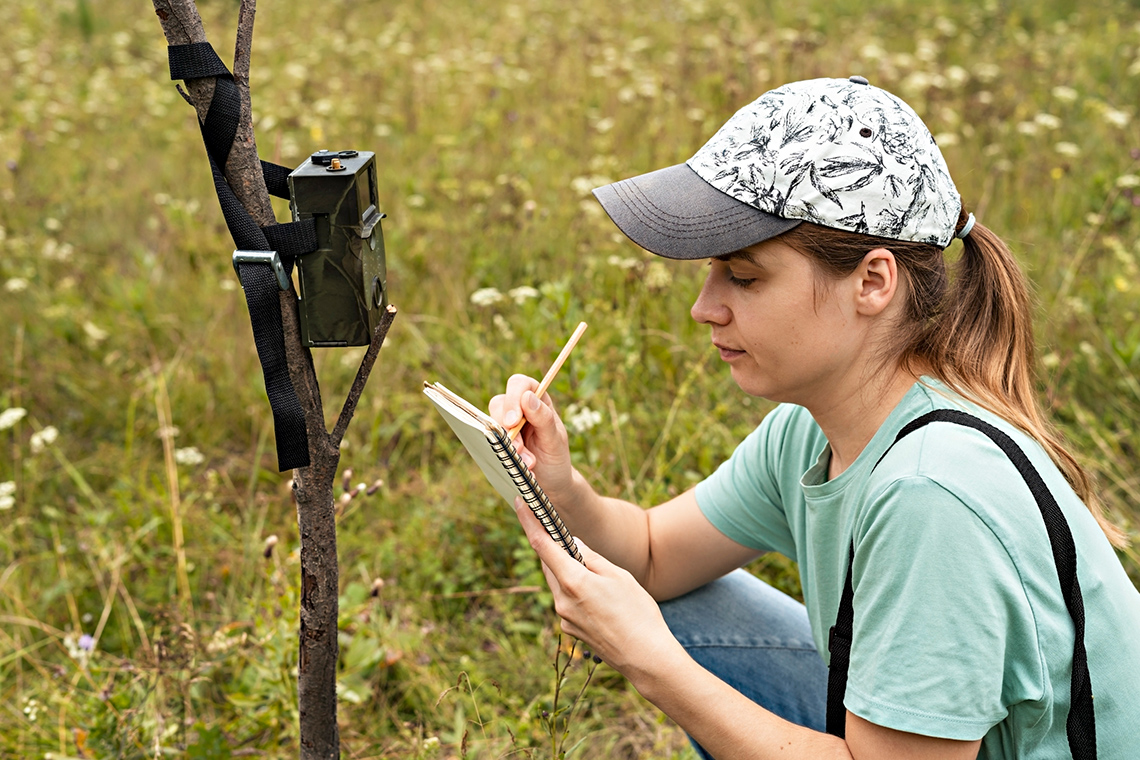 A person recording information in a notebook while kneeling down in the tall grass.