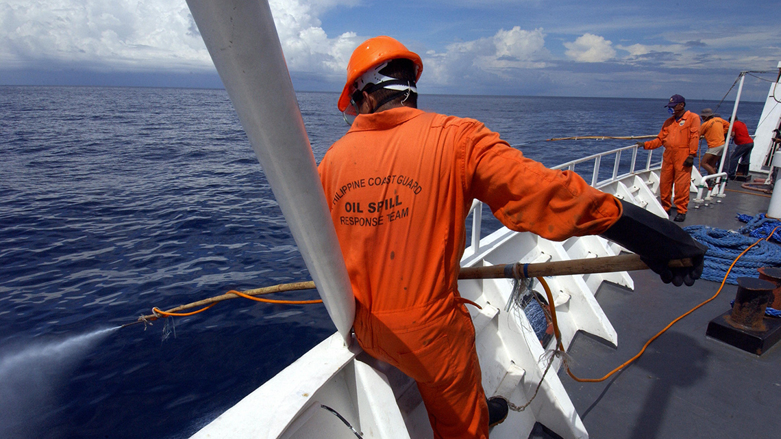 People working in a large boat, holding rods over the railing and into the water. 