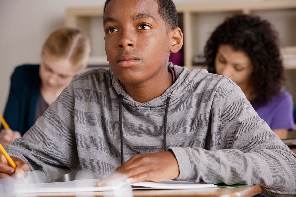 A student looking up to the front of the class while writing in their notebook.