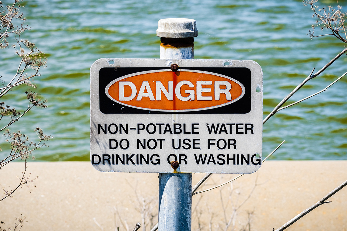 A sign beside a body of water reads “Danger. Non-potable water. Do not use for drinking or washing”.