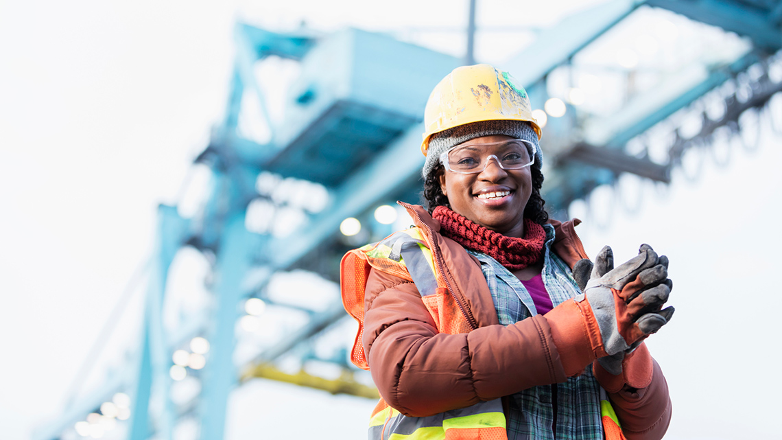 A woman with a hard hat and other protective equipment, working at a construction site.