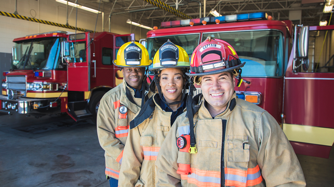 Three firefighters in front of several fire trucks.