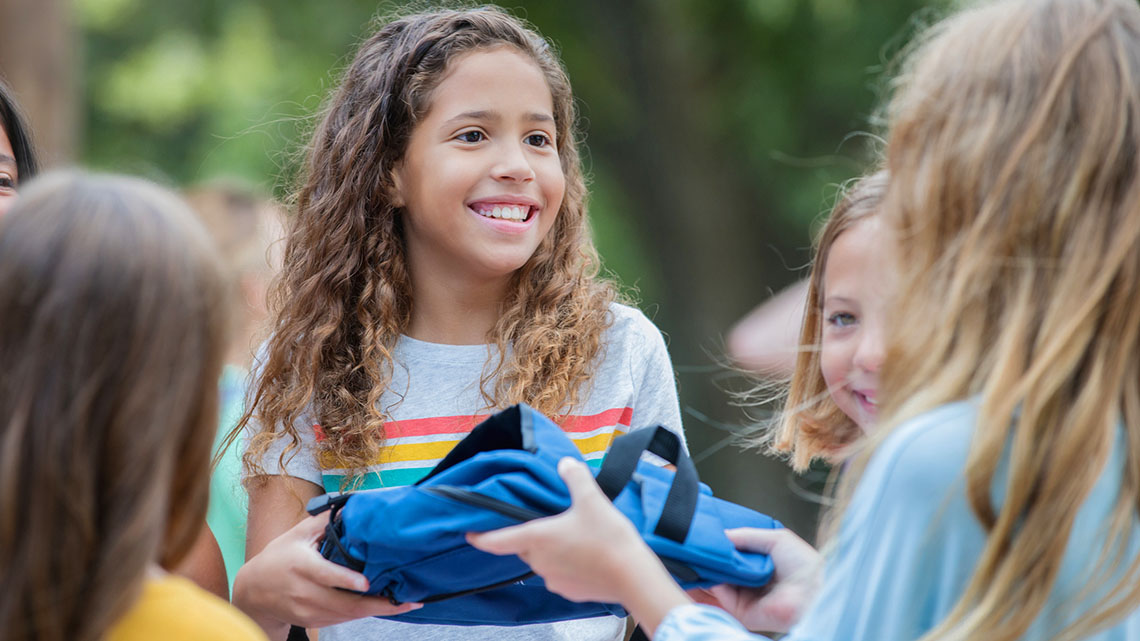 Image of kid handing a backpack to another kid.