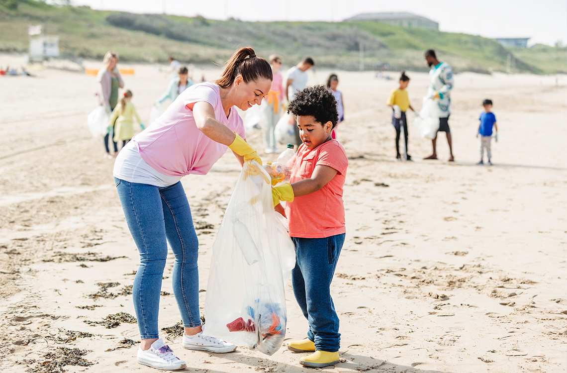 An adult with a child cleaning up garbage on a beach.