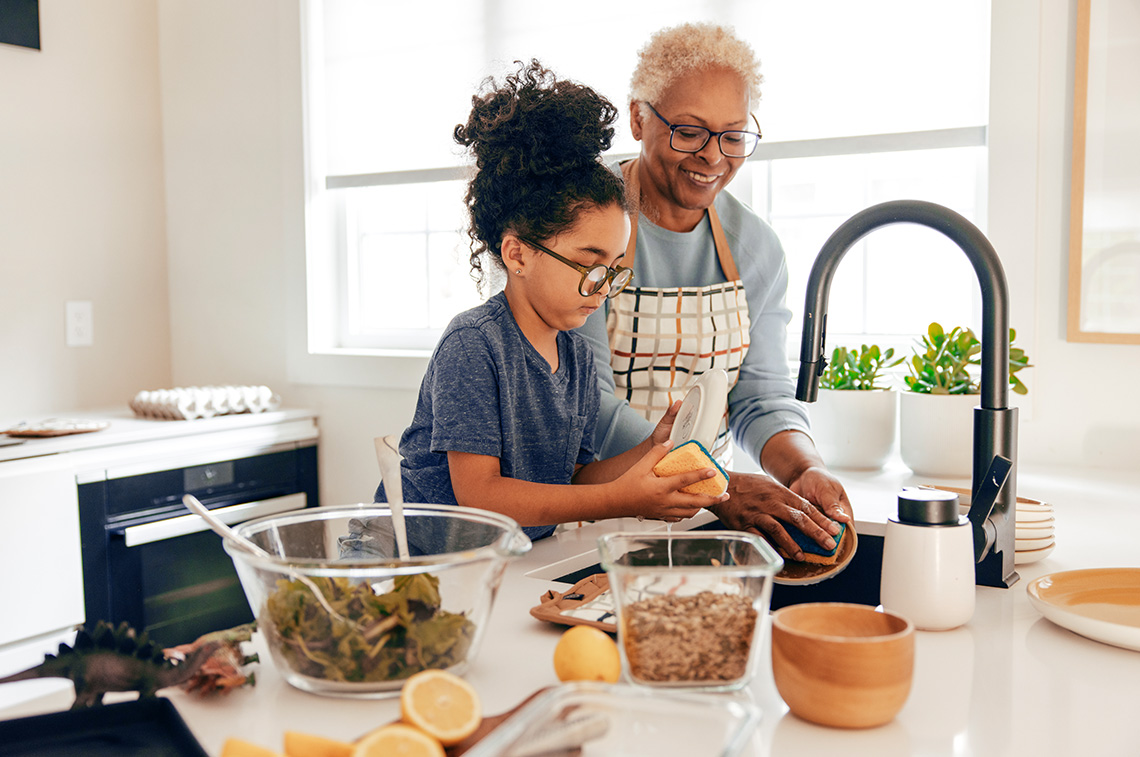 An adult and a child work together in a kitchen, preparing food beside bowls of vegetables and other ingredients.