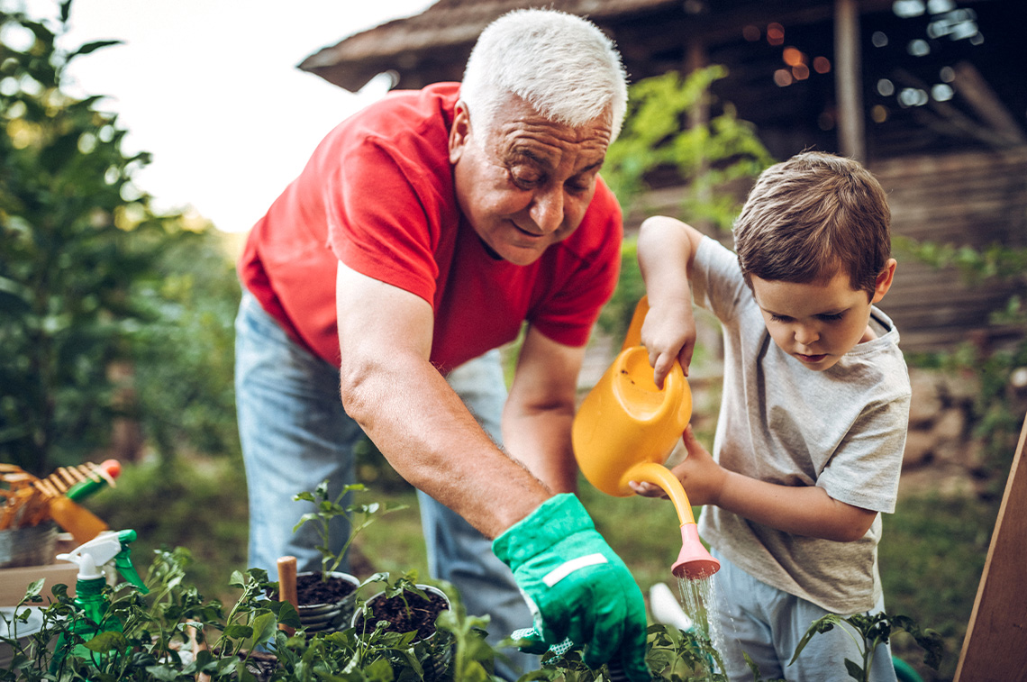 An adult and a child water plants and work among garden beds in a garden.
