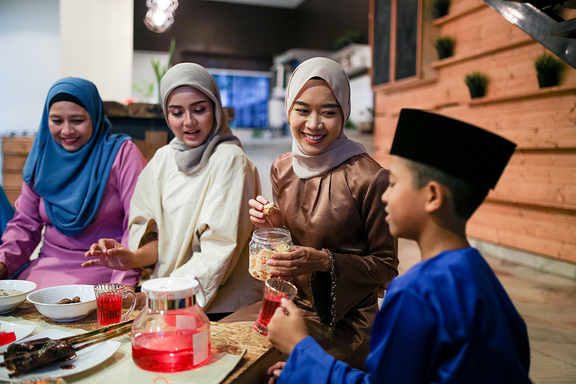 Family sitting around a spread of food at nighttime. Their hands are open in prayer.