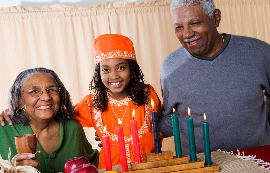 Grandpa, grandma, and child are celebrating Kwanzaa. Seven candles sit in a stand on the table.