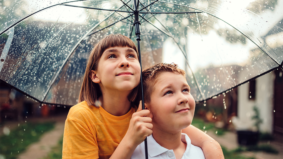 Two kids standing under an umbrella