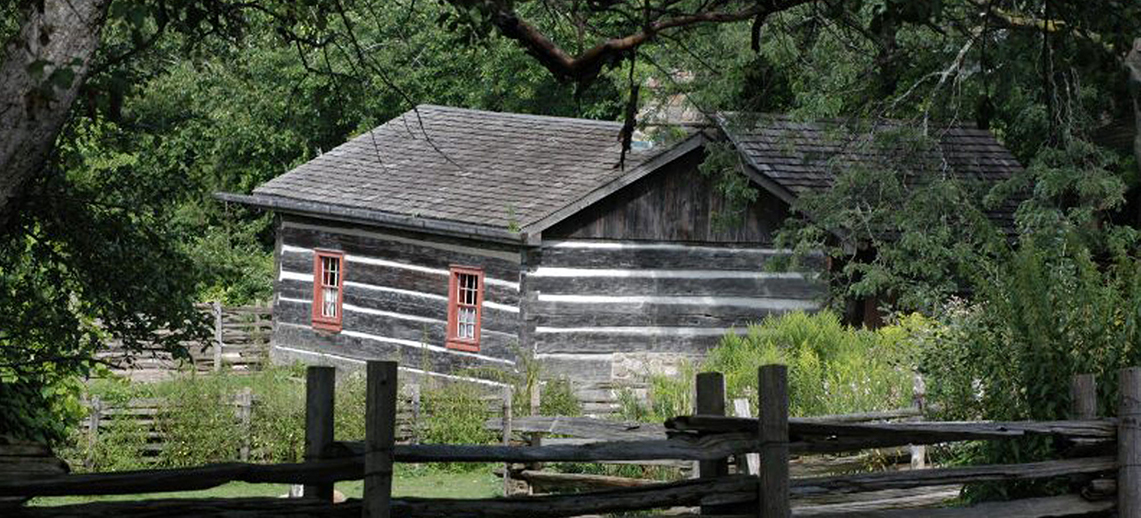 Log cabin with people outside doing chores.
