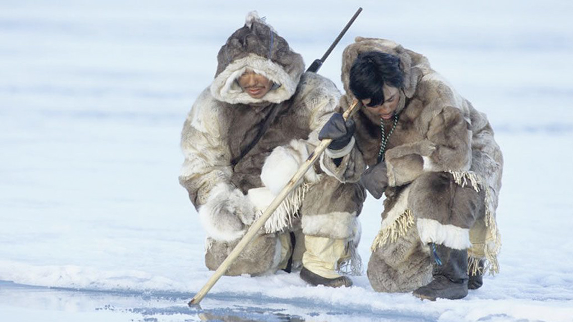 Inuit men in Nunavut, Canada, hunting by the ice in their traditional regalia.