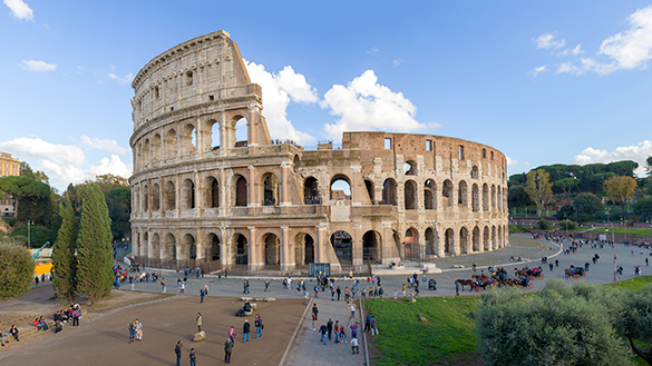 A circular building, the Colosseum, with 4 levels of arches from the ground up, and many tourists.