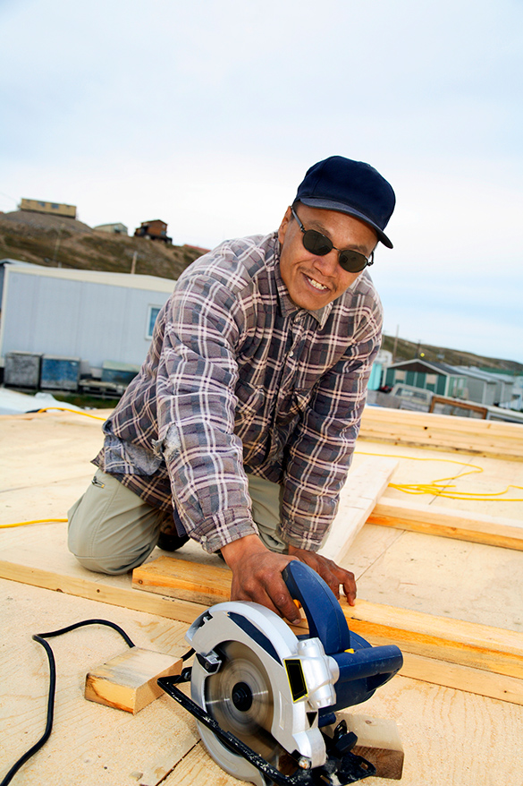 A construction worker is measuring and cutting wood using an electric saw outside in the Arctic.