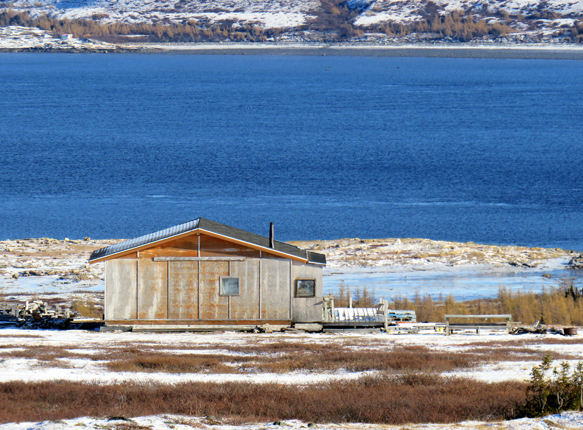 A wooden cabin by a blue river in Nunavik.