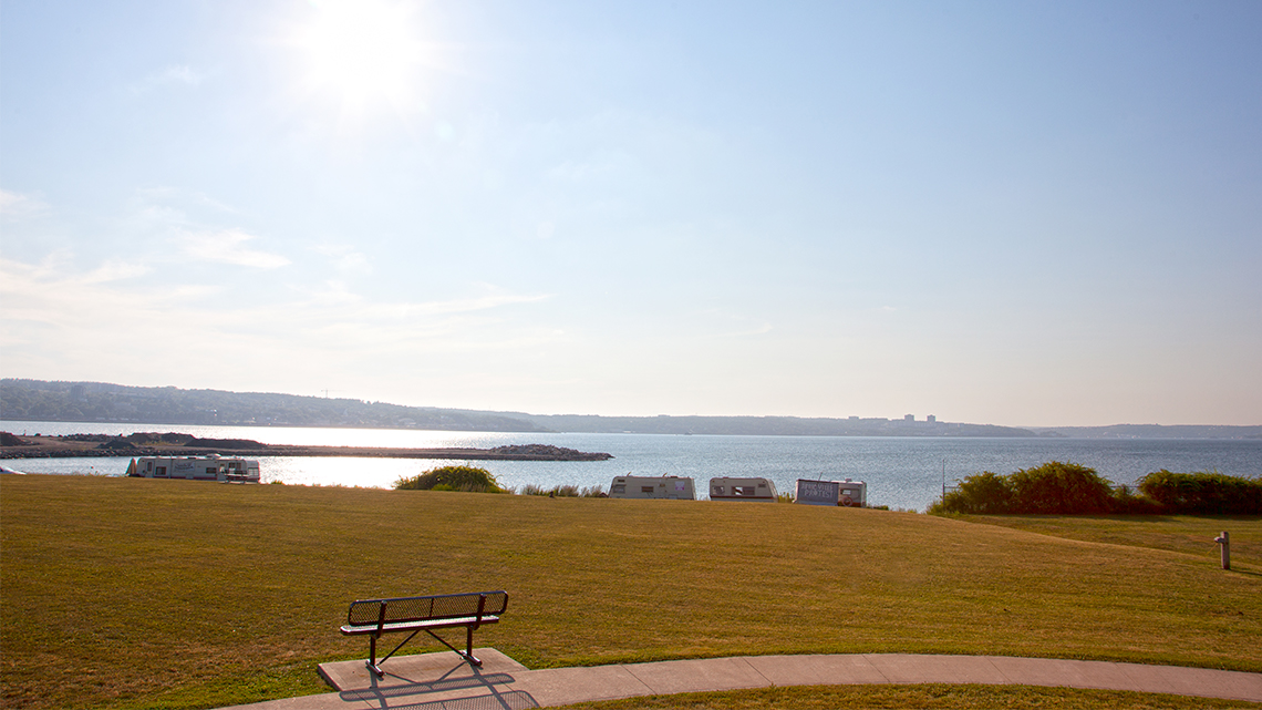 An image of a park bench and a green lawn in front of water, where Africville used to be