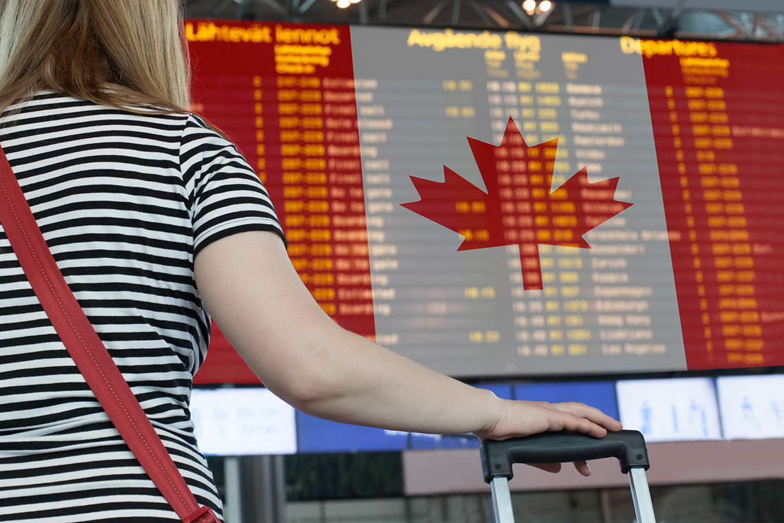 A person with luggage is examining a list of arriving flights at a Canadian airport.