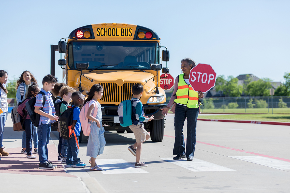 A crossing guard holding a stop sign in front of a school bus.