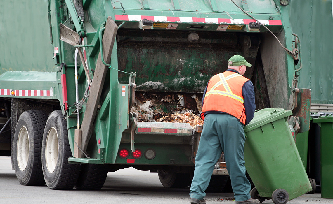 A sanitation worker collecting garbage and placing it at the back of a garbage truck for disposal.