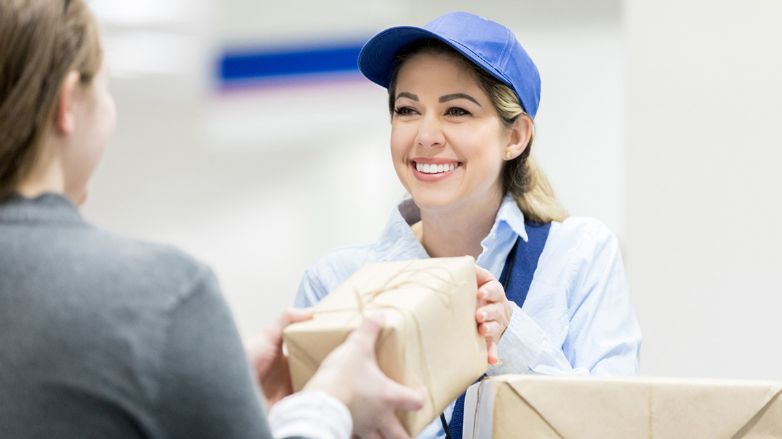 A person in a post office handing a package over to a postal worker.