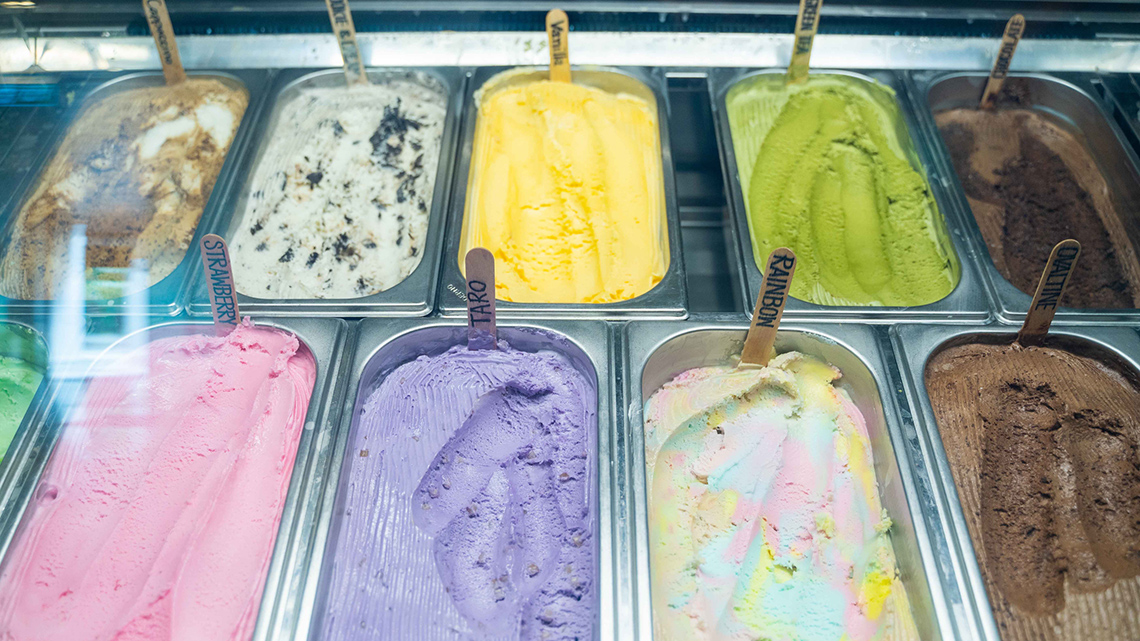 Two rows of ice cream behind a glass counter. 