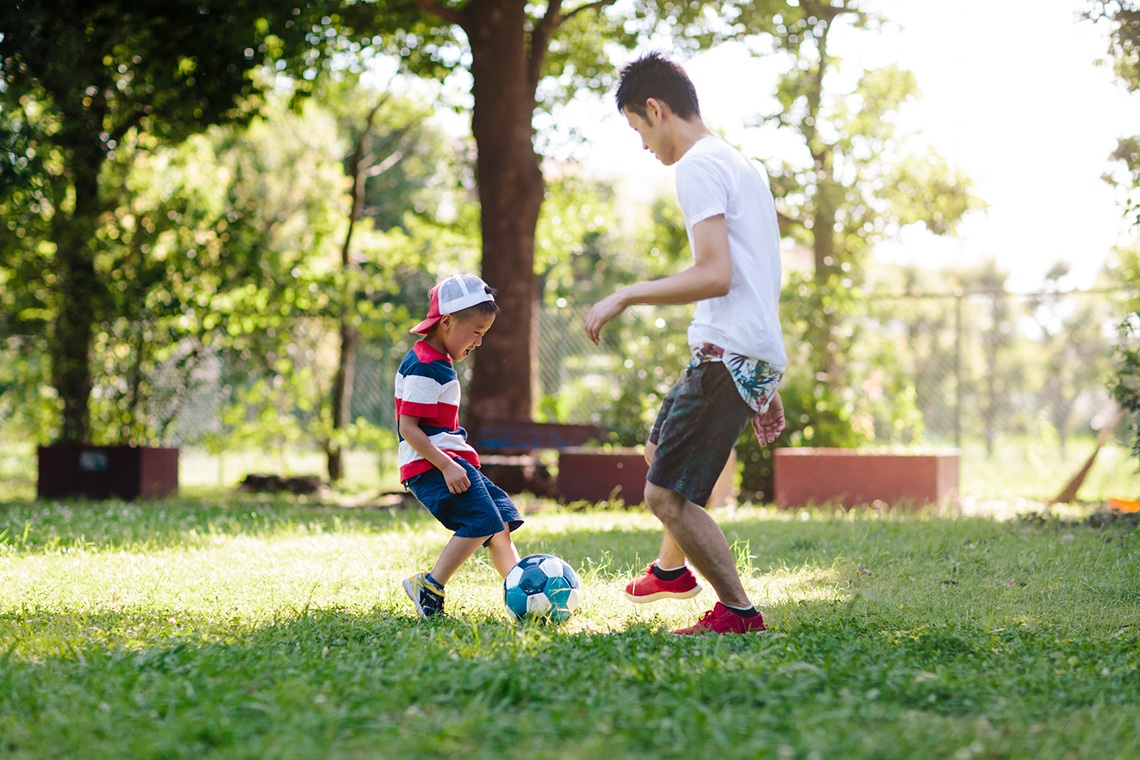 A young child and adult playing catch with a ball in a park.