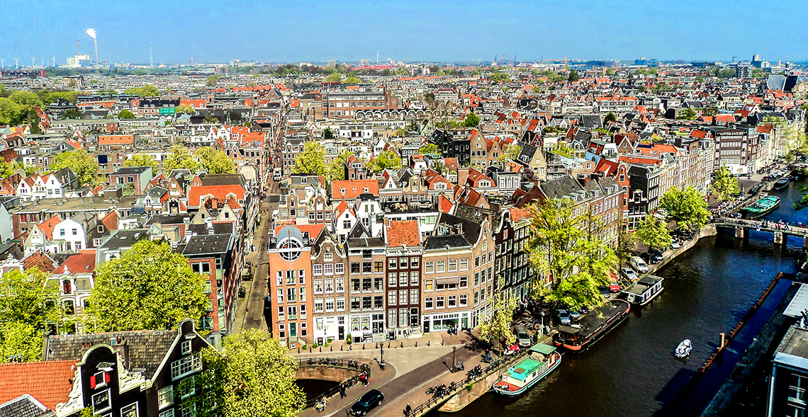 This image has many buildings and homes that are next to each other. There is also a river with small boats to transport people.