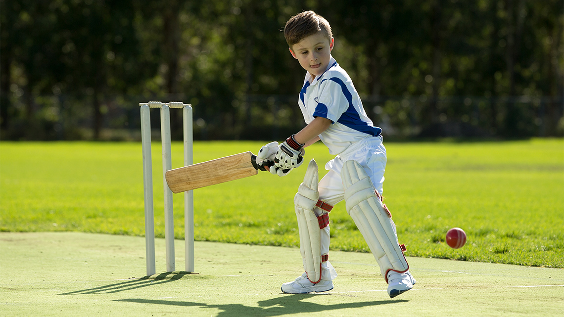 A child playing cricket. They are holding a bat and getting ready to hit the ball.
