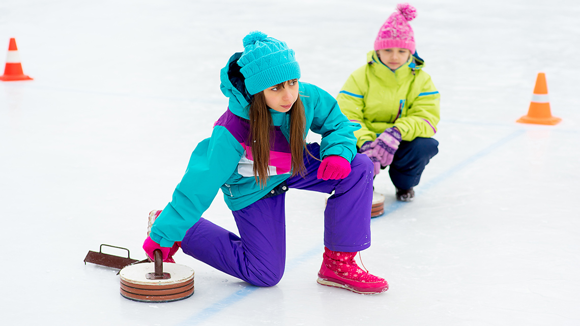 Two youths are playing curling on an ice rink.