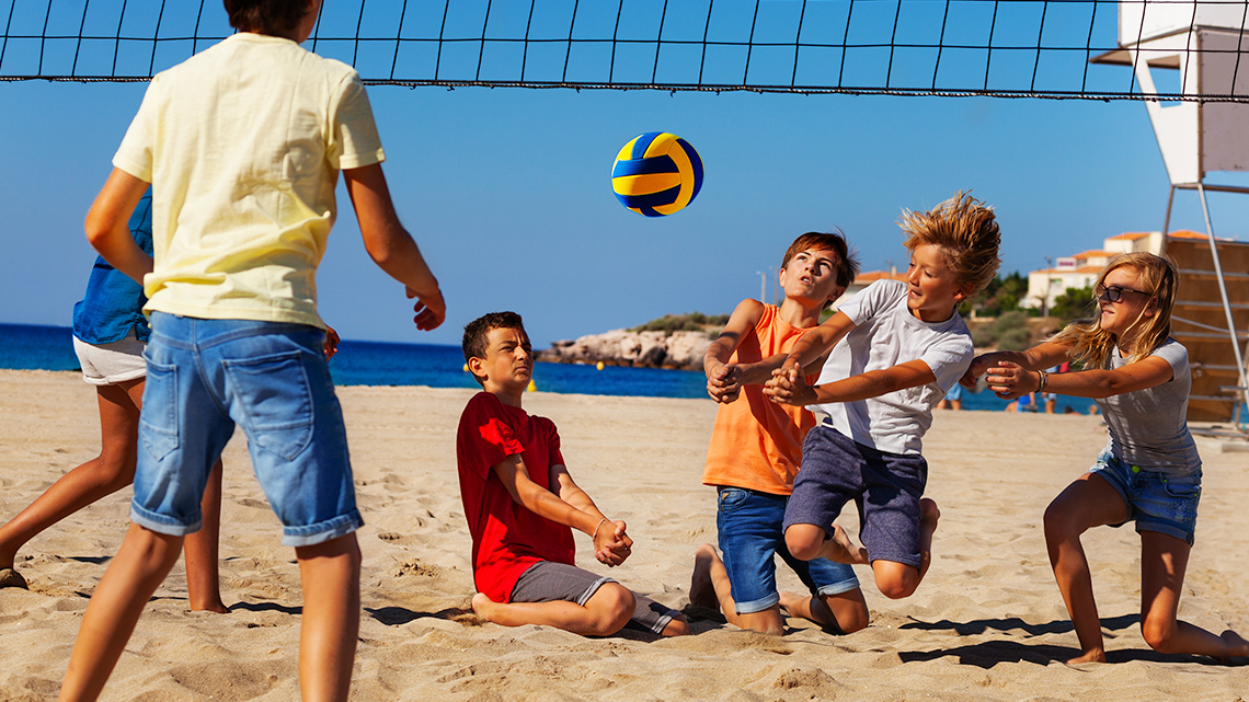 A group of school age kids playing beach volleyball.