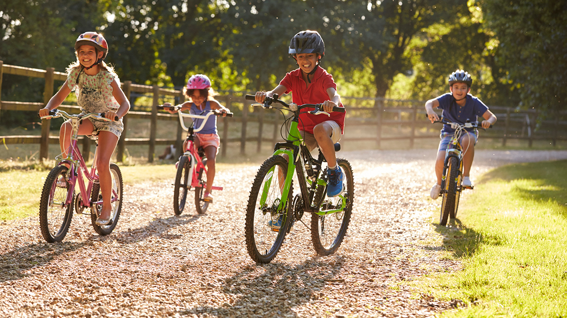 Four school age children are riding bikes together on a path.