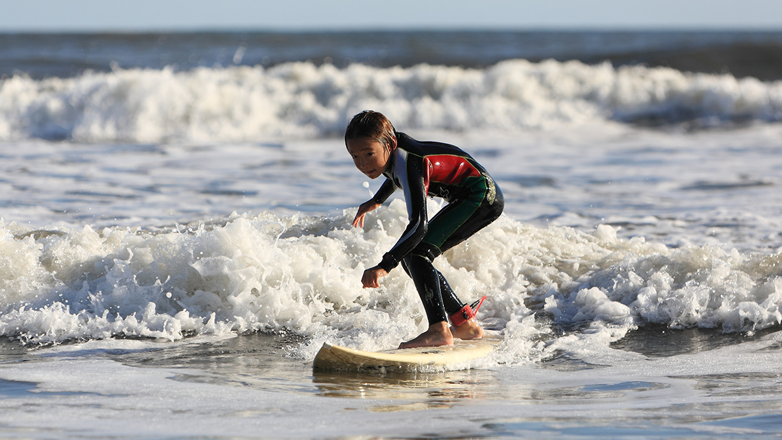 A school age child surfing in the ocean.