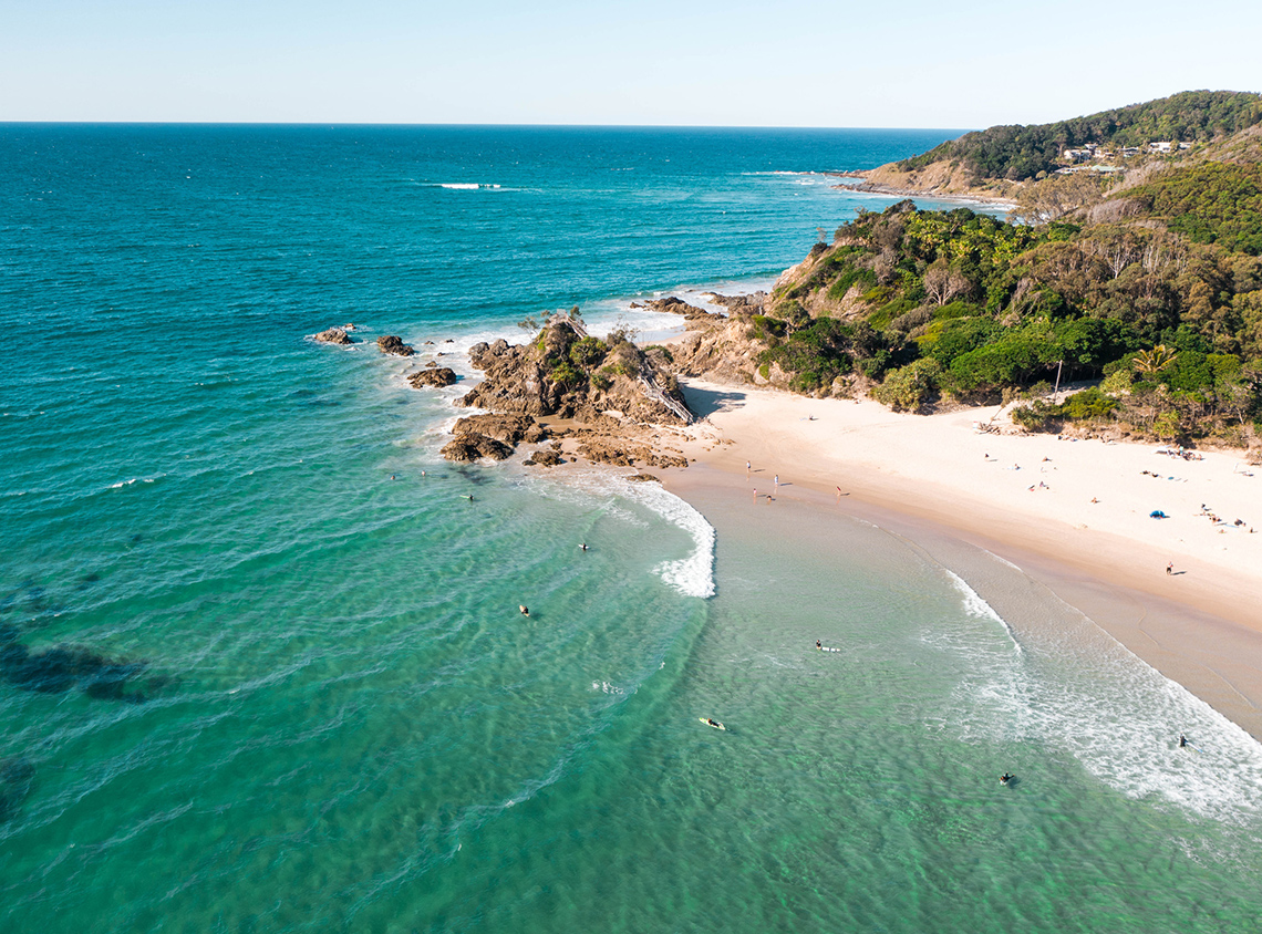 Byron Bay in Australia. The picture shows a sunny and sandy beach with clear water.
