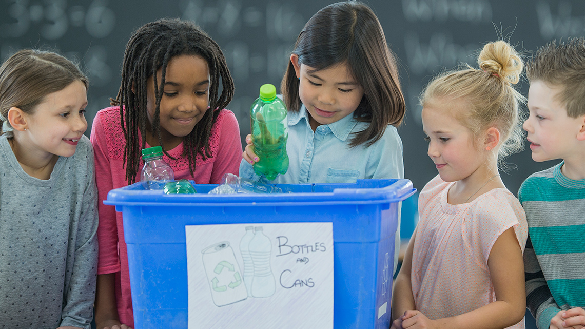Five children checking out a recycle bin that has empty plastic bottles in them.